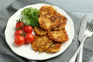 Delicious potato pancakes with tomatoes and parsley served on gray wooden table, closeup