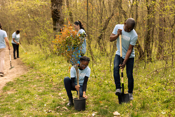 African american activists digging holes and planting trees in the woods, doing litter cleanup and...