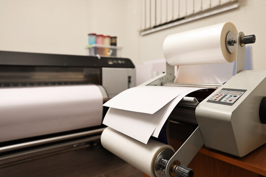 Modern roll laminator with paper on desk indoors. Printing house