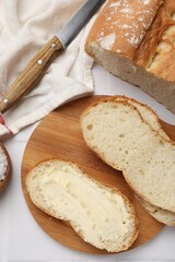 Fresh bread with butter and knife on white tiled table, flat lay