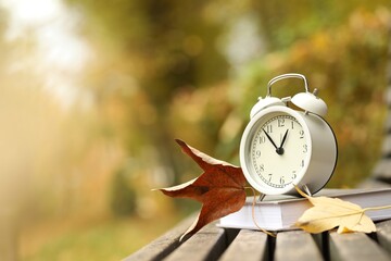 Autumn time. Alarm clock and book on bench in park, closeup. Space for text