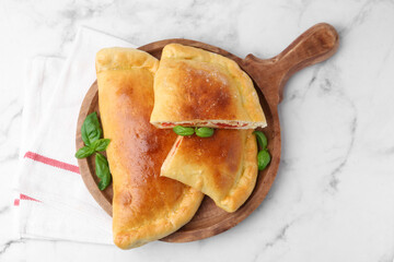 Tasty vegetarian calzones with tomato, cheese and basil on white marble table, top view