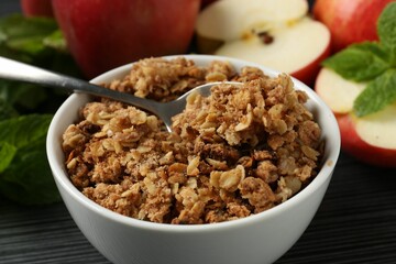 Delicious apple crisp in bowl, fresh fruits and mint on black textured table, closeup