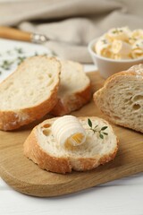 Cut baguette with butter and herbs on white wooden table, closeup