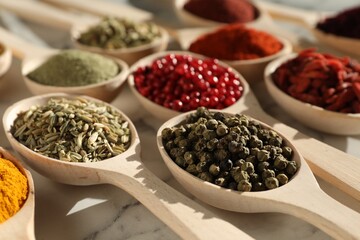 Different aromatic spices in spoons on white marble table, closeup