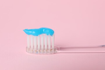 Toothbrush with toothpaste on pink background, closeup