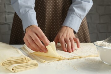 Woman with puff pastry dough at white table, closeup