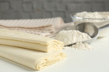 Raw puff pastry dough on white table, closeup. Space for text