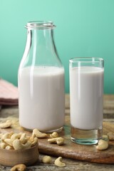 Fresh cashew milk in glass, bottle and nuts on wooden table against green background, closeup