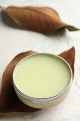 Natural solid perfume in container and dry leaves on white table, closeup