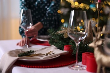 Woman setting table for Christmas dinner at home, focus on plate, cutlery and decor
