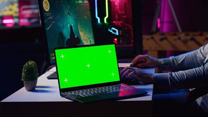 Green screen laptop next to man playing with friends online, shooting asteroids together in...
