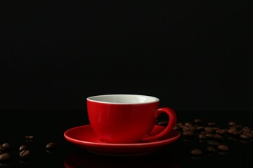 Red cup with coffee and roasted beans on black background, space for text