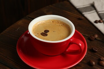 Red cup with coffee and roasted beans on wooden table, closeup