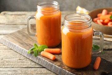 Fresh carrot juice in mason jars, vegetables and mint on wooden table, closeup