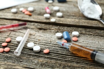Drug addiction. Syringe and pills on wooden table, closeup