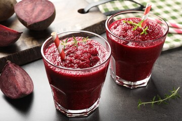 Fresh beetroot smoothie in glasses and cut vegetables on grey textured table, closeup