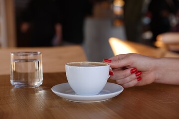 Woman with cup of aromatic coffee at wooden table in cafe, closeup