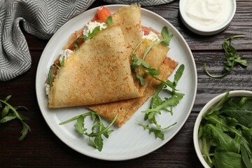 Delicious crepes with salmon, cream cheese and arugula on wooden table, flat lay