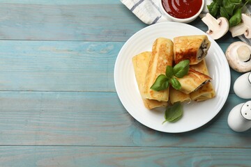 Delicious rolled crepes with mushrooms, basil and sauce on light blue wooden table, flat lay. Space for text