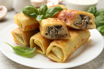 Delicious rolled crepes with mushrooms and basil on grey table, closeup