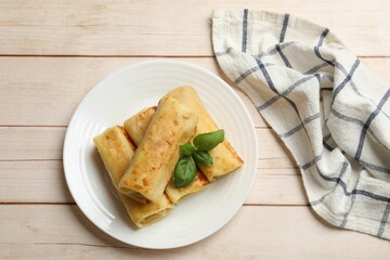 Delicious rolled crepes with basil on wooden table, top view