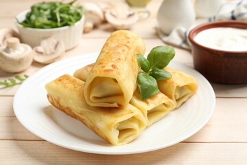 Delicious rolled crepes with basil, mushrooms and sour cream on wooden table, closeup