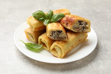 Delicious rolled crepes with mushrooms and basil on grey table, closeup