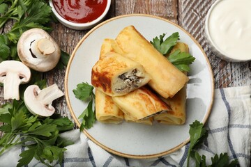 Delicious rolled crepes with mushrooms, parsley, sour cream and sauce on wooden table, flat lay