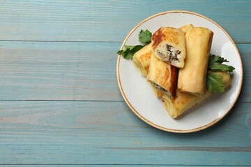 Delicious rolled crepes with mushrooms and parsley on light blue wooden table, top view. Space for text