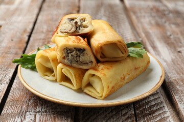 Delicious rolled crepes with mushrooms and parsley on wooden table, closeup