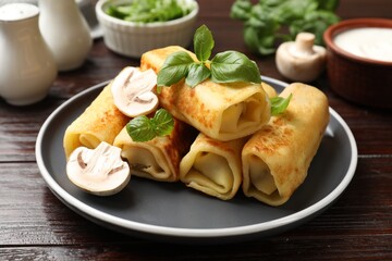 Delicious rolled crepes with mushrooms and basil on wooden table, closeup