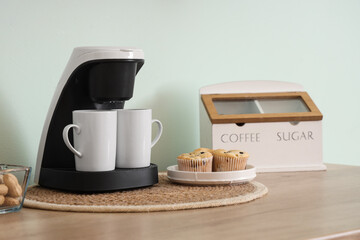 Coffee machine with cups and muffins on counter in kitchen, closeup
