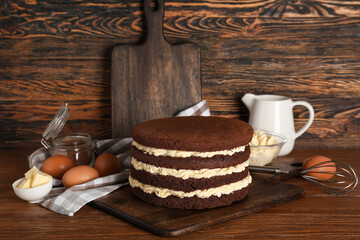 Tasty sponge cake, fresh ingredients and utensils on wooden background