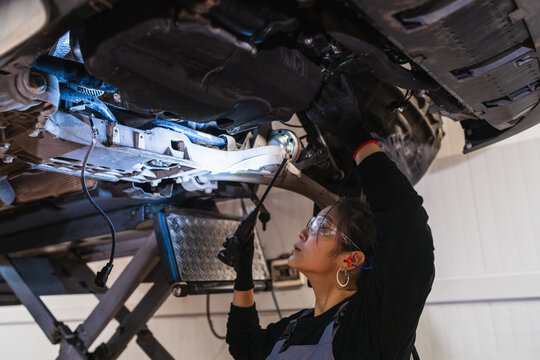 Female chinese mechanic inspecting car's undercarriage in repair shop