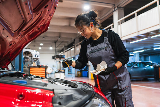 Female chinese mechanic checking oil level of red car in garage - Powered by Adobe