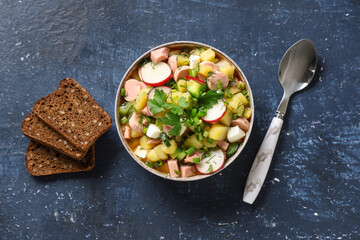Bowl of tasty okroshka, spoon and bread on color background