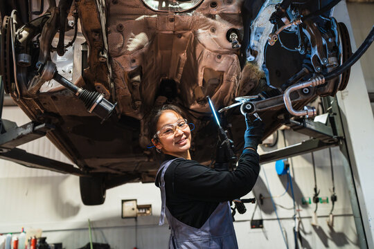 Female chinese mechanic repairing car chassis in auto repair shop - Powered by Adobe