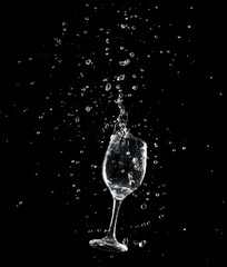 Pouring Clear Wine glass with spilled water liquid in air. Water soda splashing out of glass with curve spill and splashing. Black background isolated element