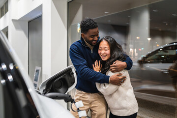 Happy couple hugging in electric car dealership, embracing sustainable mobility