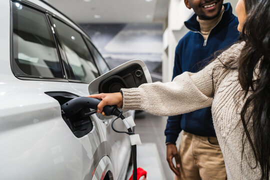 Woman charging electric car with couple in dealership