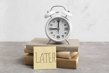 Paper sheet with word LATER, stack of books and alarm clock on grunge table