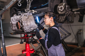 Female chinese mechanic inspecting gearbox with light in auto repair shop