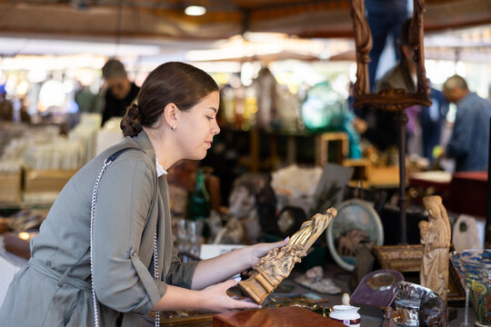 Smiling female tourist checking out handcrafted wooden statuette at flea market