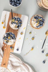 Three healthy blueberry Lemon Overnight Oats topped with blueberries, lemon zest and coconut shavings on a light blue wooden counter. Top view