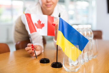 Preparation for international negotiations. Female office coordinator setting national flags of...