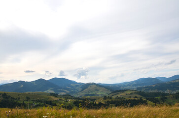 Serene view of rolling hills and distant mountains beneath an expansive sky filled with soft clouds. Perfect for evoking peace and tranquility in natural and rural settings. Carpathians, Ukraine