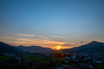 Picturesque sunset over a serene Verkhovyna village nestled in rolling hills, capturing calmness...