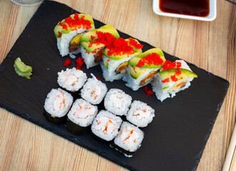 Assorted different types of sushi served with bowl of soy sauce on board in restaurant