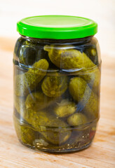 Image of glass jar with pickled cucumbers on wooden background